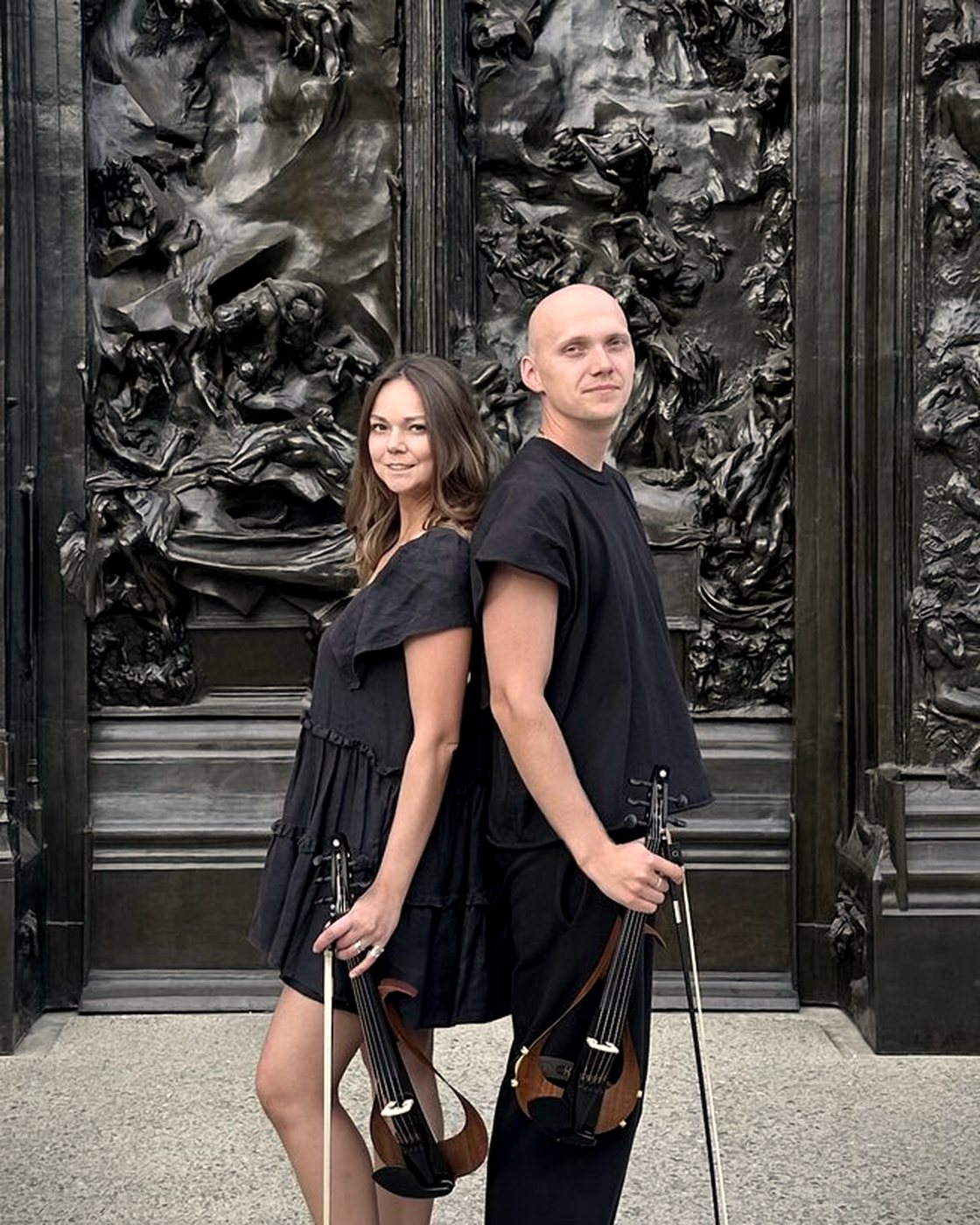 Nadezhda and Anton standing back to back with electric violins in front of Rodin's Gates of Hell
